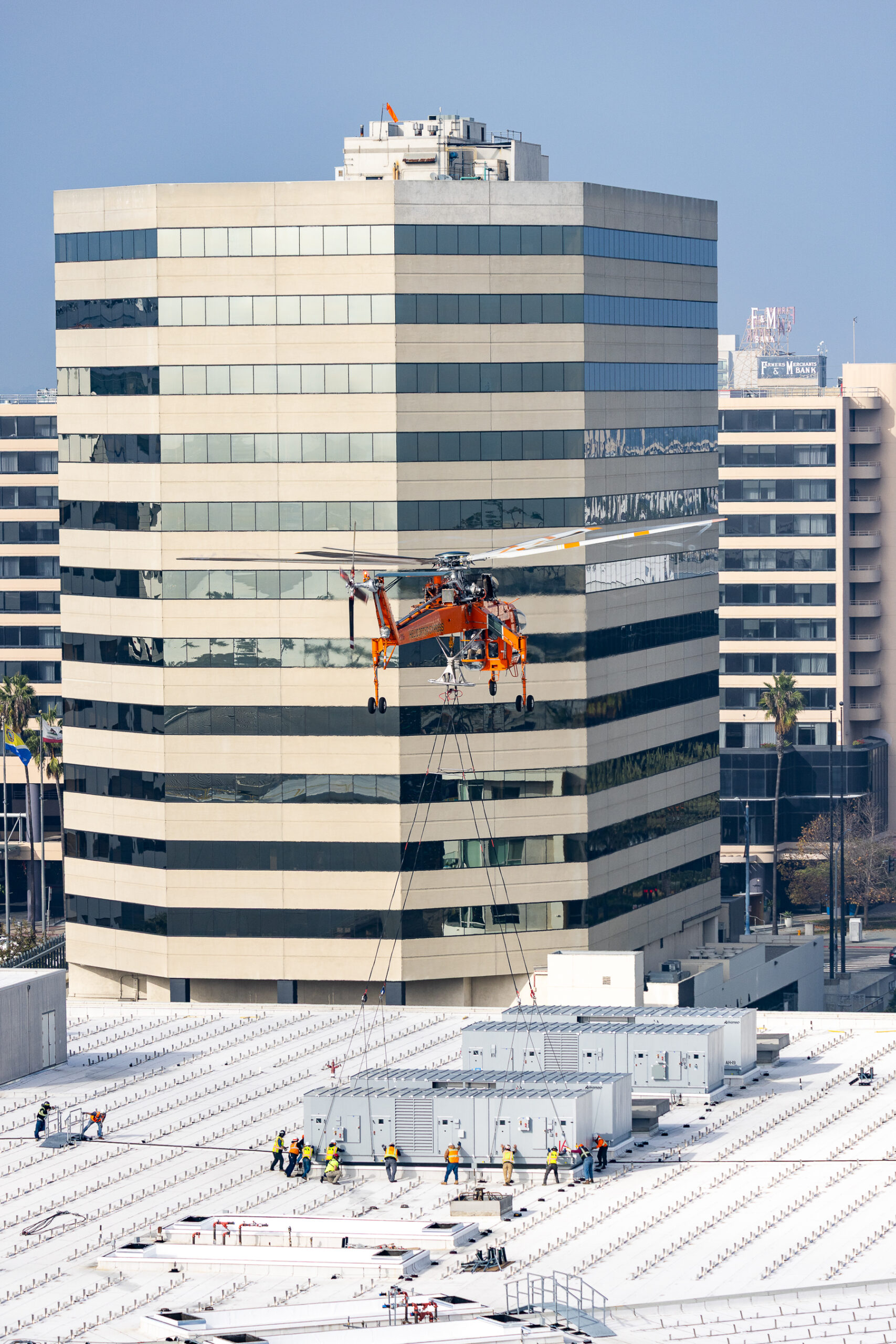 helicopter lowers structure onto roof where workers wait below